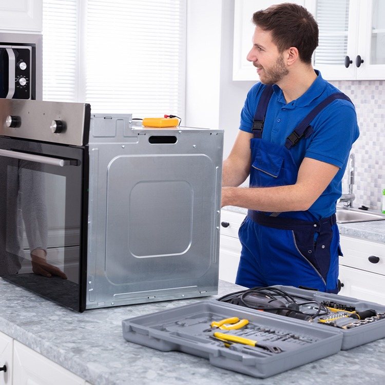 Appliance technician kneeling by an oven with a Hapric set screw kit open on the floor